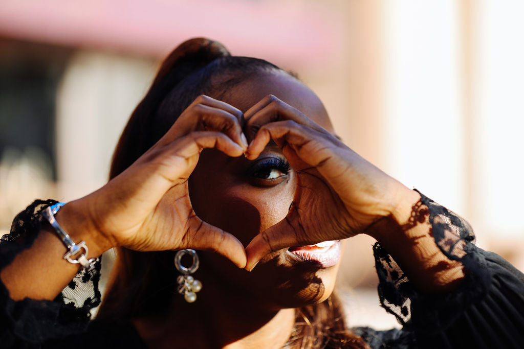 Person making a heart shape with their hands outdoors