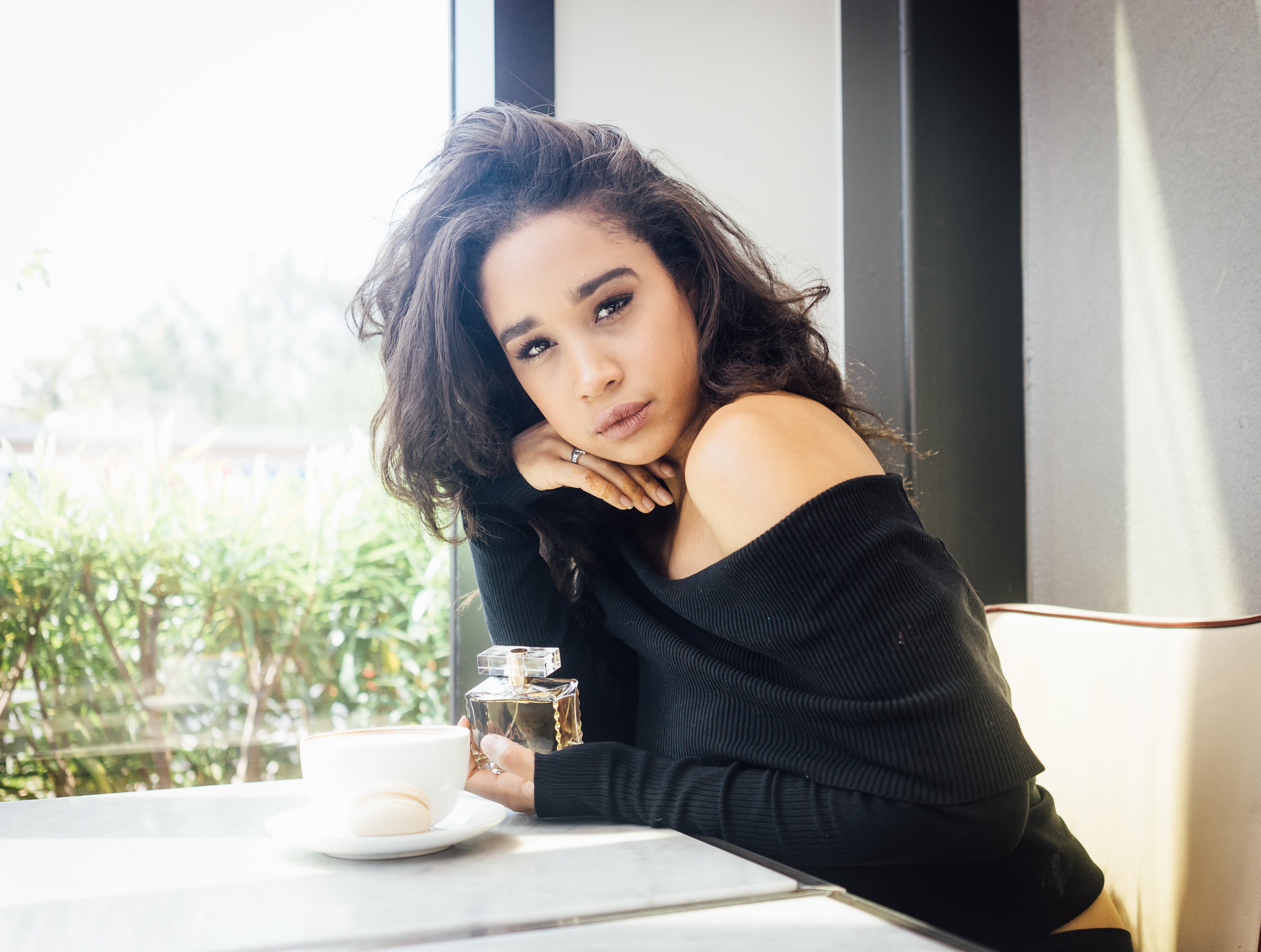 Woman sitting at a table with a cup and bottle, looking out a window.